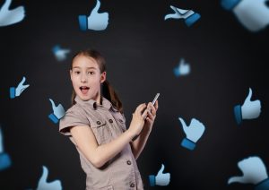Children addiction to social networks. Portrait of little girl surprised touching screen of mobile phone at black background. Child and thumb up icons fly around. New generation device, communication